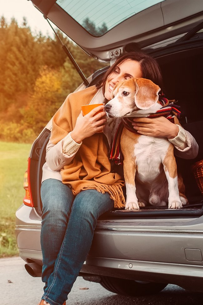 Frau sitzt mit ihrem Hund auf der Kofferraumkante